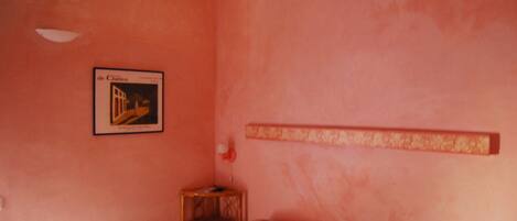 A bedroom with a bed, a small wooden nightstand, a framed picture on the wall, and a decorative wall panel.