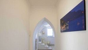 Ein Flur mit Holzboden, weißen Wänden, einer Deckenleuchte und einer Treppe, die zu einer oberen Ebene führt.