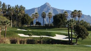 Un parcours de golf avec des bunkers de sable, des palmiers et une montagne en arrière-plan.
