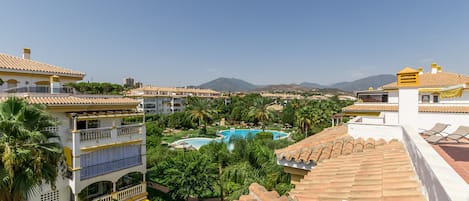 A resort with a swimming pool surrounded by lush greenery and palm trees, overlooking a mountainous landscape.