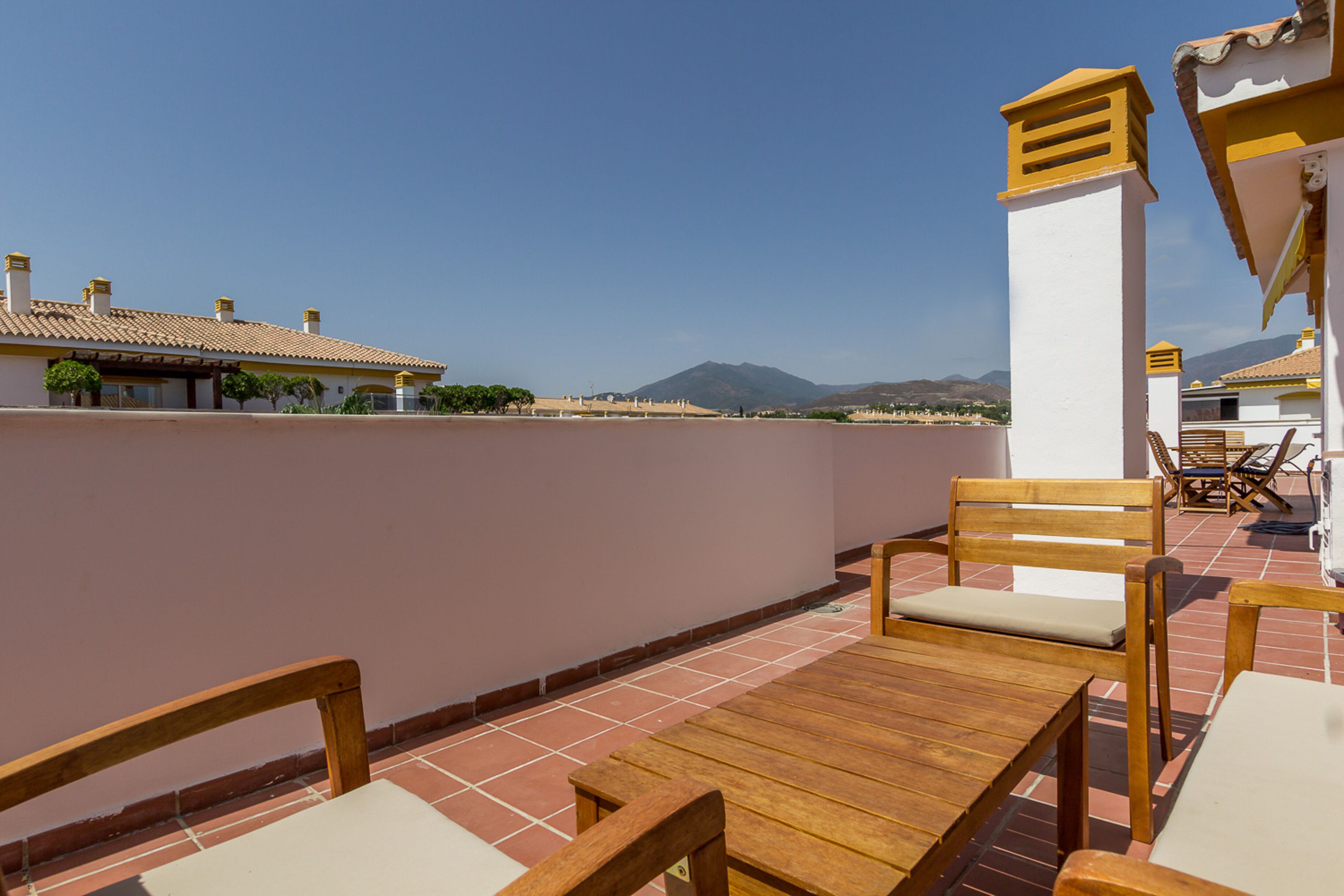 A terrace with wooden furniture and a view of distant mountains.
