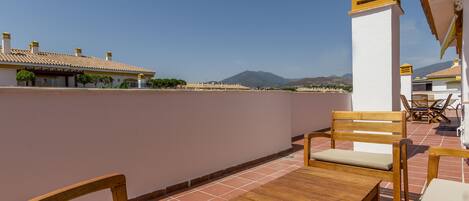 A terrace with wooden furniture and a view of distant mountains.