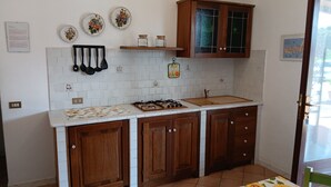 A kitchen with wooden cabinets, a gas stove, and a sink. There are decorative plates on the wall and a small shelf with jars. - Villa Giuliana, Two-room apartment 4 Ptl. (Capoliveri)