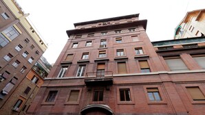 A multi-story building with a brick facade, multiple windows, and a central entrance with an archway. - ROMAC - Trinity (Rome)