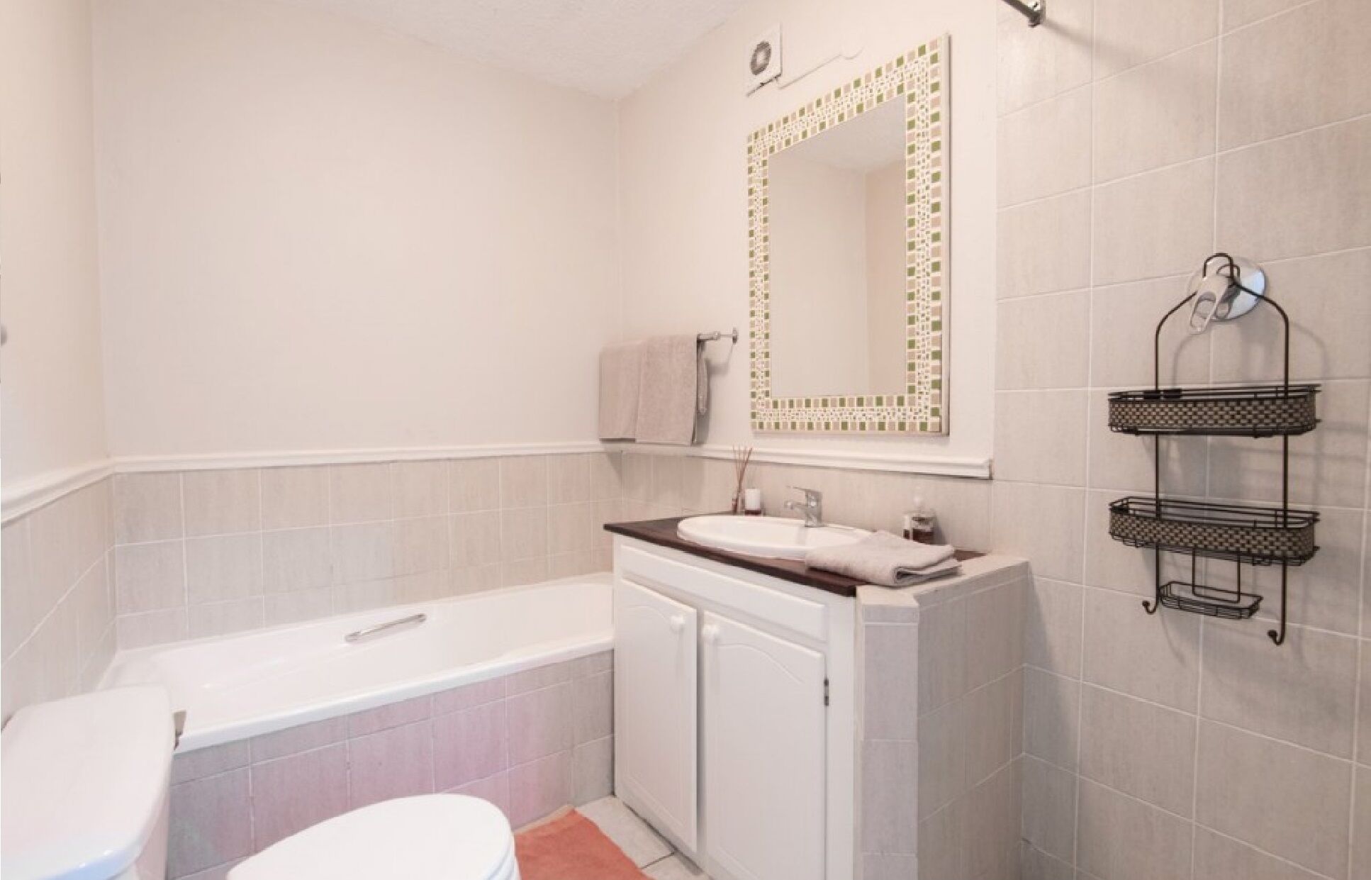A bathroom with a white bathtub, a sink with a mirror above it, and a towel rack with a towel hanging on it.