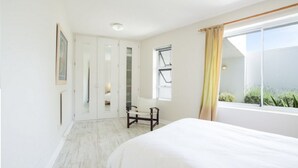 Een slaapkamer met een bed, een bureau, een stoel, een kledingkast en een raam met gordijnen.