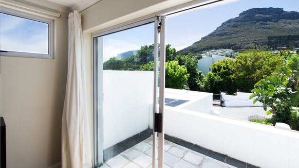 Een balkon met een glazen deur die uitkomt op een terras, met uitzicht op een bergachtig landschap en een wateroppervlak.