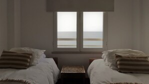 Een slaapkamer met twee bedden, een raam met uitzicht op zee en een klein tafeltje tussen de bedden.