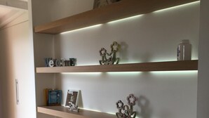 A modern interior with three wooden shelves, each illuminated by under-shelf lighting. A clock and decorative items are displayed on the top shelf.