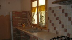 Una cocina con salpicadero de ladrillo, una ventana con cortinas florales, un lavamanos y una estufa a gas.