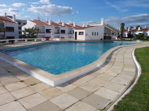 Uma piscina com um deck ladrilhado, rodeada por edifícios brancos com telhados vermelhos.