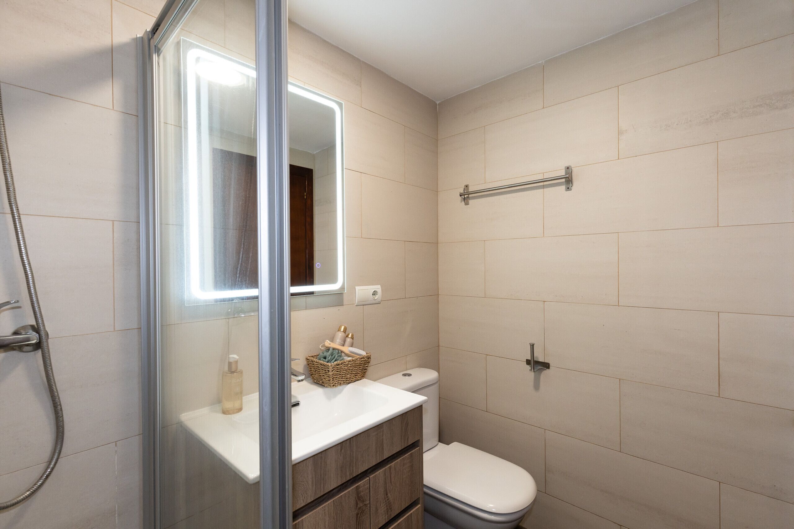 Une salle de bain avec une douche à parois de verre, un lavabo blanc, des toilettes et un miroir avec éclairage.