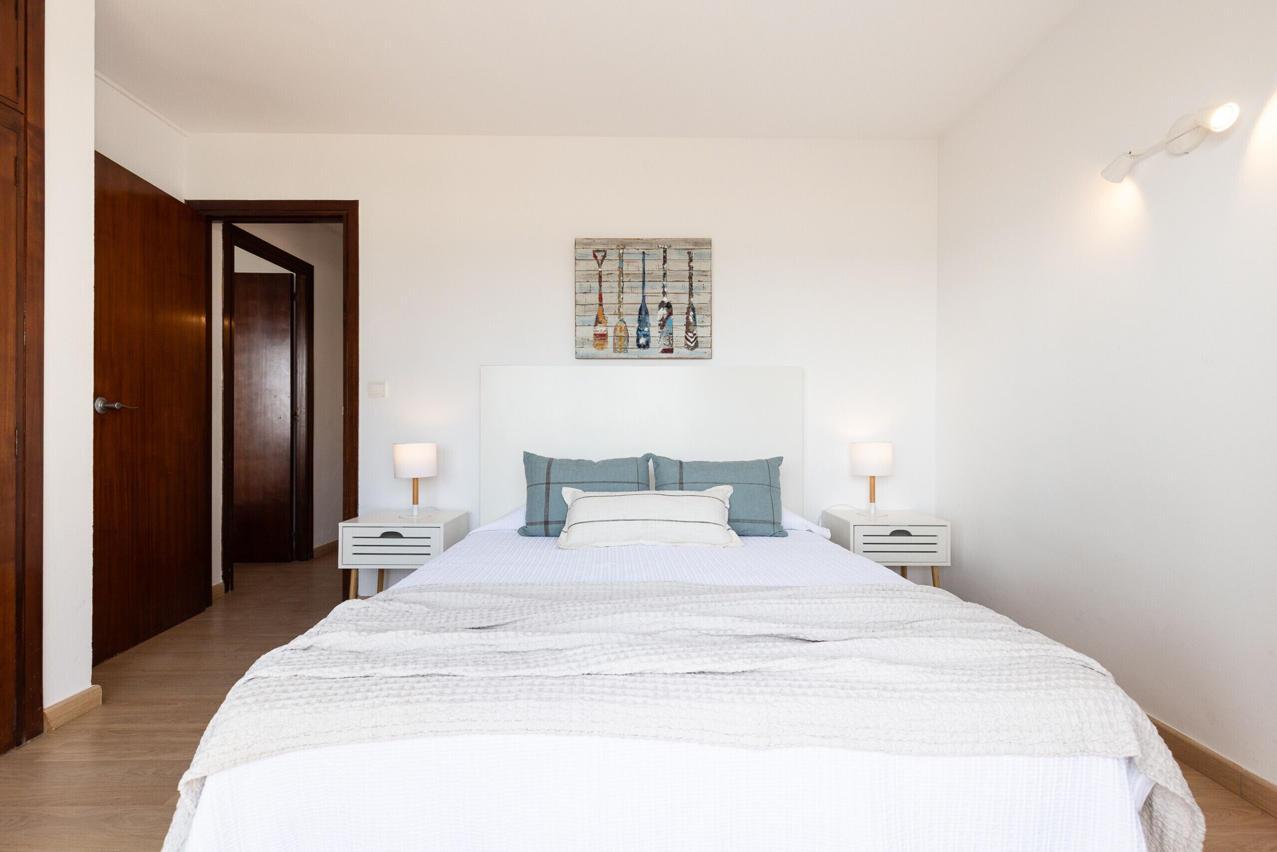 Een slaapkamer met een bed, nachtkastje, wanddecoratie en een deur.