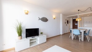 Un salon moderne doté d’un téléviseur à écran plat, d’un coin repas avec une table et des chaises en bois, et d’appliques murales décoratives.
