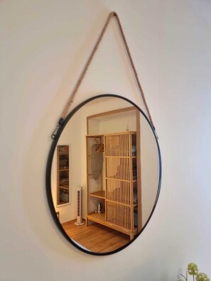 A circular mirror with a wooden frame hanging on a wall, reflecting a room with a wardrobe, a radiator, and a small plant.