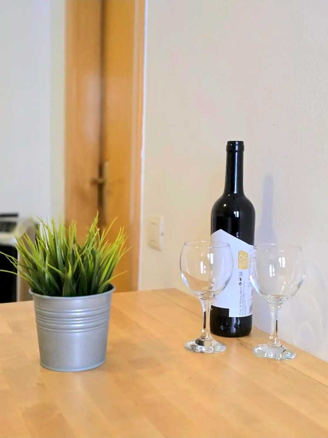 A bottle of wine, two wine glasses, and a potted plant on a wooden table.