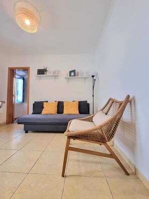 Ein Zimmer mit einer Couch, einem Korbsessel und zwei Regalen mit Gegenständen.