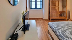 Een slaapkamer met een bed, een bureau met een computer, een spiegel, een raam en een kledingkast.