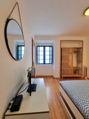 Une chambre à coucher avec un lit, un bureau avec un ordinateur, un miroir, une fenêtre et une armoire.