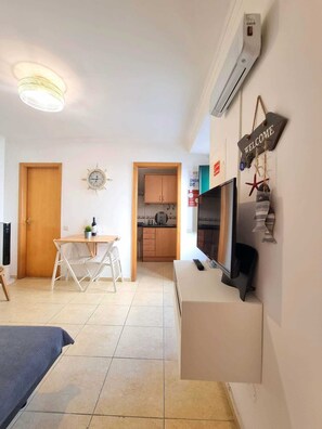 A compact living space with a kitchenette, a dining area, a TV, and a 'WELCOME' sign.