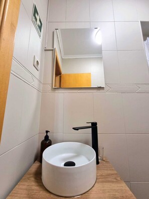 Un baño con un lavabo blanco redondo, un grifo negro y un espejo encima.