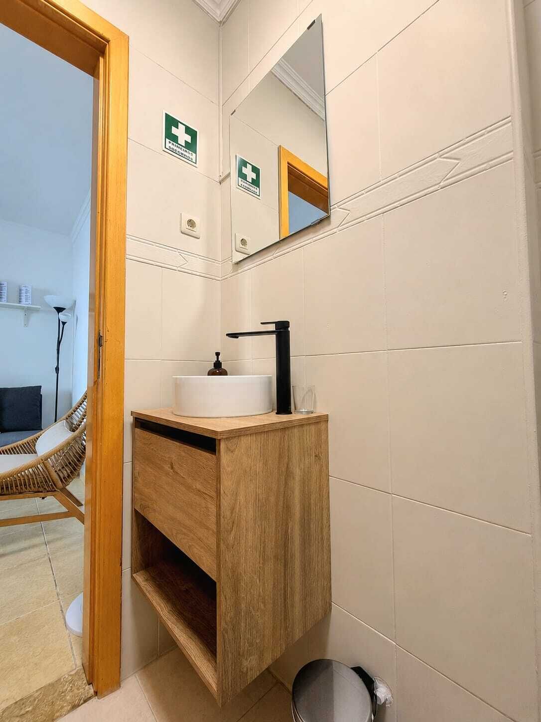Uma casa de banho com toucador de madeira, pia branca, torneira preta e espelho sobre a pia.