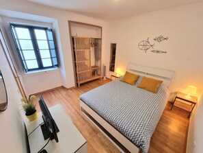 Ein Schlafzimmer mit Bett, Nachttischen, Schreibtisch, Kleiderschrank und Fenster.