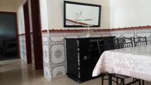 A dining area with a table set for two, a black cabinet, and a patterned wall. - APARTMENT AGADIR GROUND FLOOR <br> (AGADIR)
