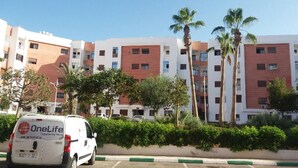 A multi-story residential building with balconies, surrounded by palm trees and greenery. - APARTMENT AGADIR GROUND FLOOR <br> (AGADIR)