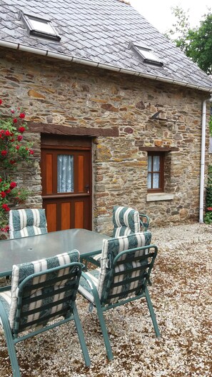 A stone building with a wooden door and window, a table with chairs, and red flowers. - Hydrangea gite one of 4 properties  (Saint-Connec)