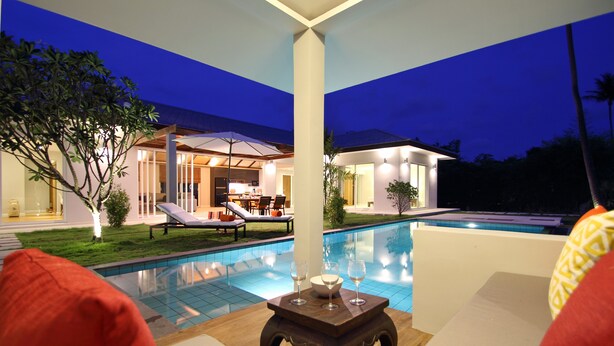 A poolside area with lounge chairs and a table, a dining area with chairs and a table, and a well-lit building with a pool. - A Luxurious Retreat in Bophut (koh samui)