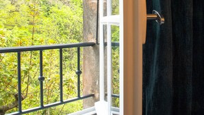 Ein Balkon mit Metallgeländer, einem Fenster und Blick auf einen grünen Wald.