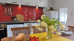 Eine Küche mit roten Fliesen, einem Holztisch, Brot, Tomaten und einer Blumenvase.