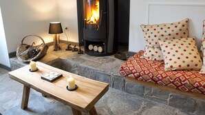 Ein gemütlicher Raum mit Kamin aus Stein, einem Holztisch mit Kerzen und einem gemusterten Sofa.