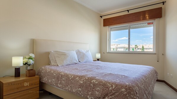 Une chambre à coucher avec un lit, des tables de chevet, une fenêtre donnant sur un beau paysage et une tête de lit en bois.