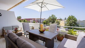 Un balcon agrémenté de meubles en osier, une table avec un saladier rempli de fruits et un grand parasol.