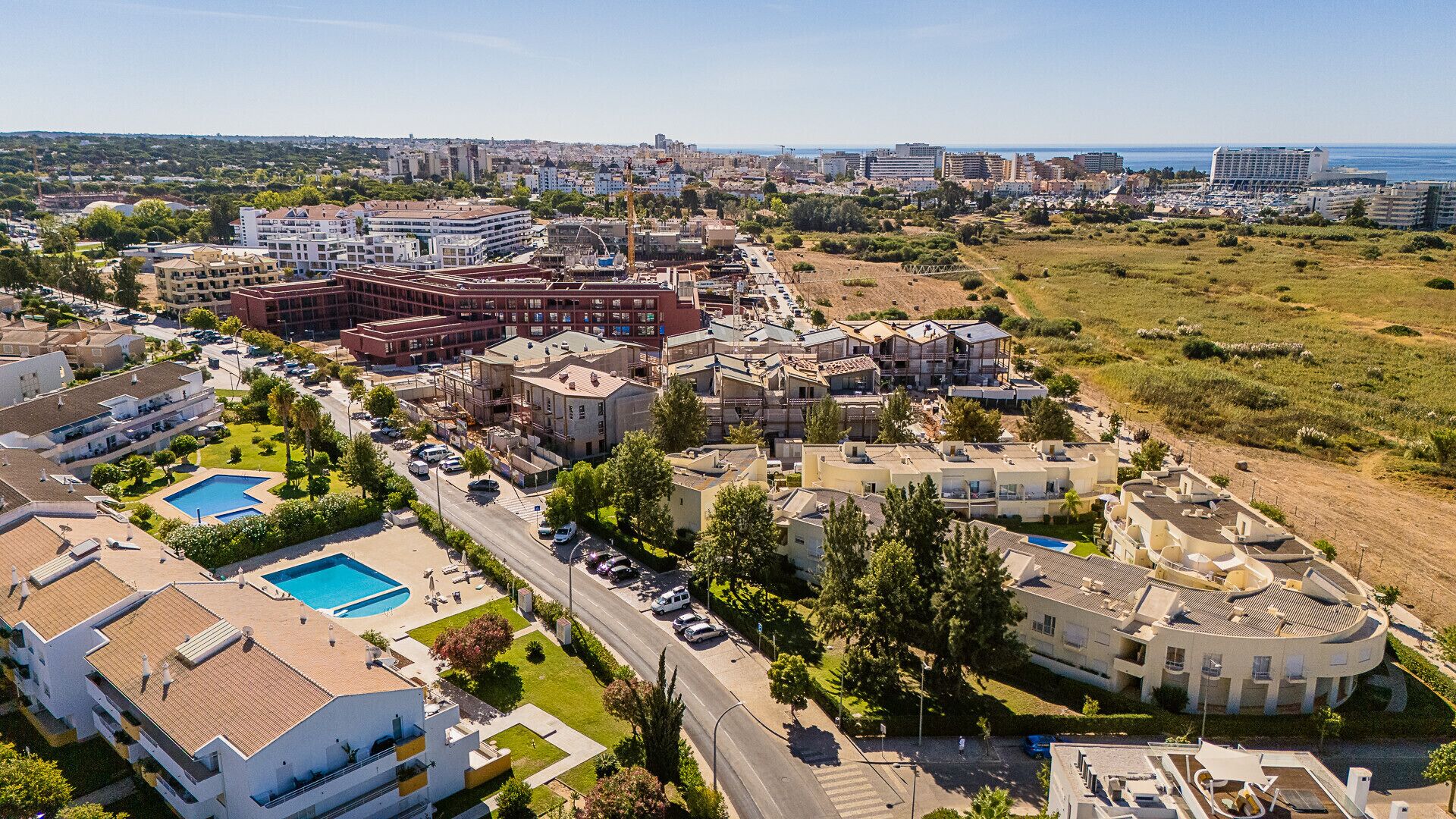 Vue aérienne d’une zone de villégiature côtière comprenant plusieurs bâtiments, dont un grand hôtel avec une piscine et un bâtiment plus petit à la forme circulaire.