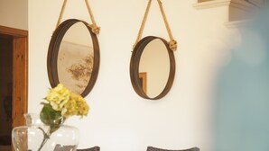Zwei ovale Spiegel hängen an einer weißen Wand, eine transparente Glasvase mit gelben Blumen steht auf einem Tisch und ein Stapel Bücher ist zu sehen.