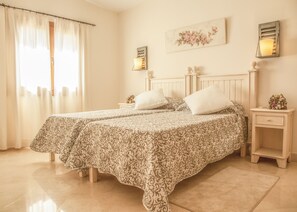 Una cama doble con ropa de cama estampada, una mesita de noche con lámpara y una decoración floral en la pared.