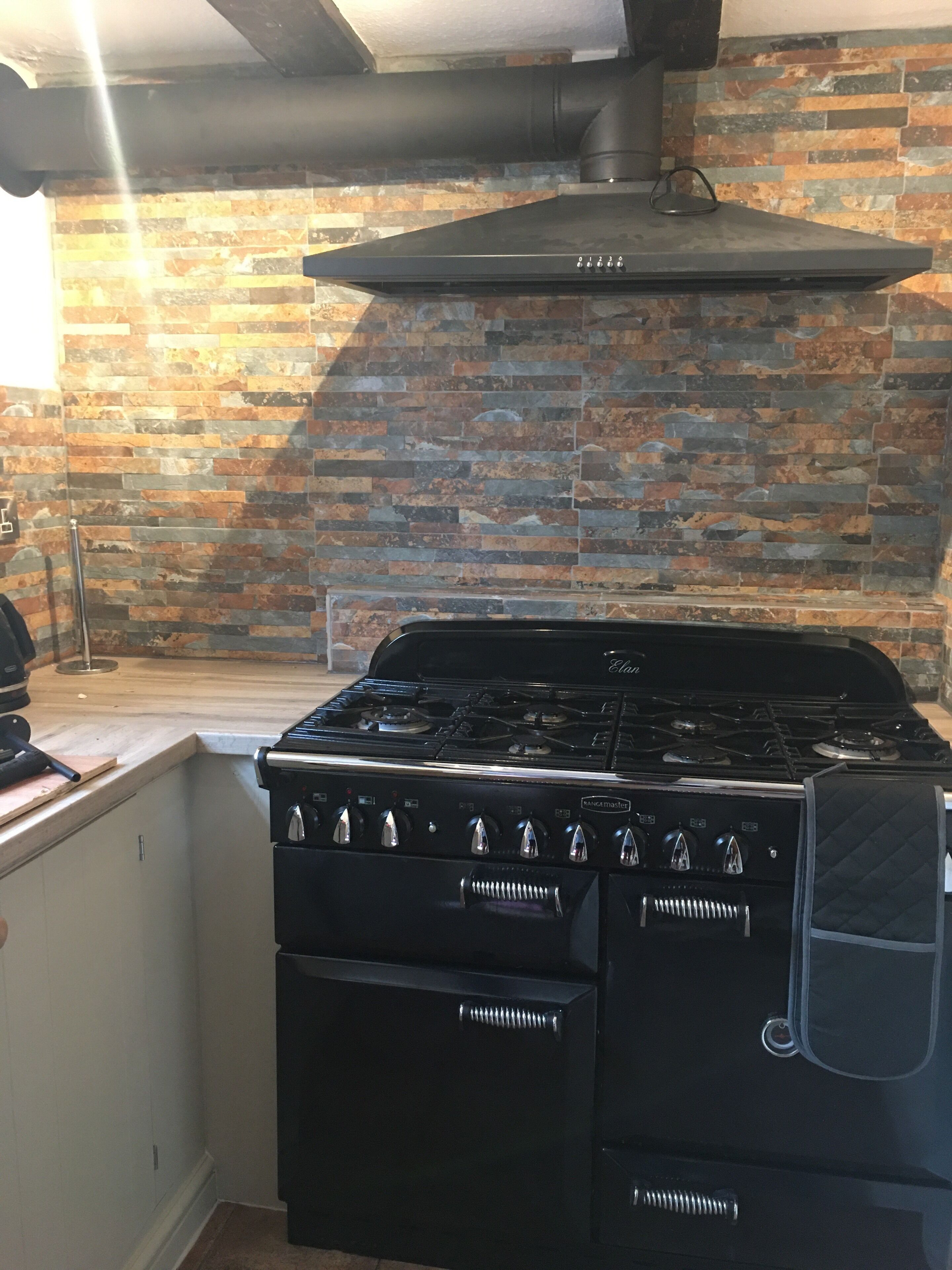 A kitchen with a black stove, oven, and chimney. It features a brick wall and a wooden countertop.