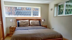 Een slaapkamer met een houten bed, twee nachtkastjes met lampen, een raam met uitzicht op gebouwen, en een houten vloer.