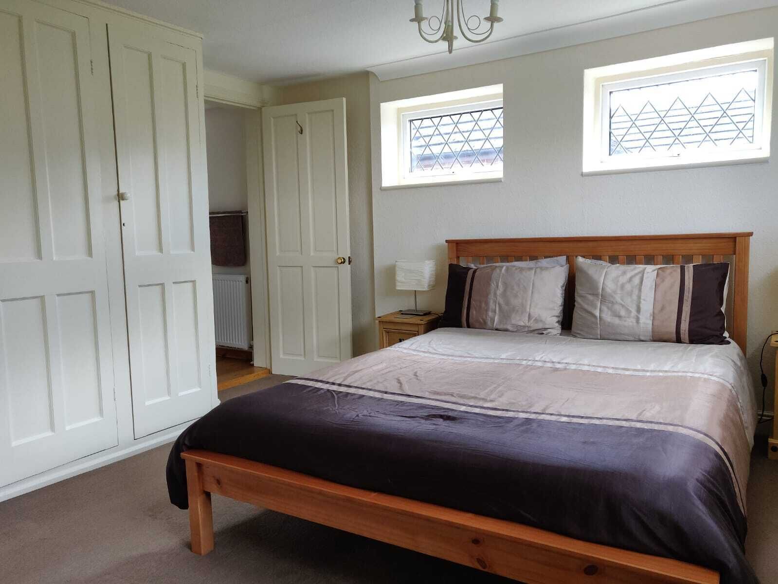 A bedroom with a wooden bed, a nightstand, a dresser, and two windows with a geometric pattern.