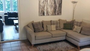 Een woonkamer met een hoekbank, een houten salontafel en een groot abstract schilderij aan de muur.