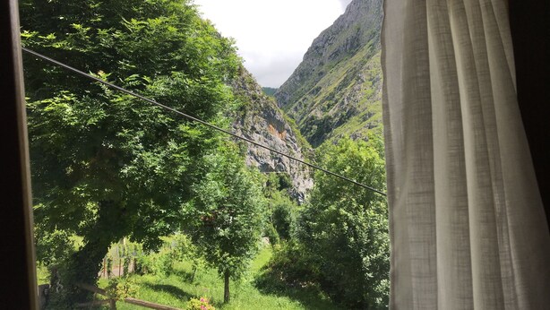 A view through a window with a curtain, featuring a lush green landscape with trees and a mountain in the background. - Natural Jacuzzi impressive Gorge in the Picos de Europa (Ponga)
