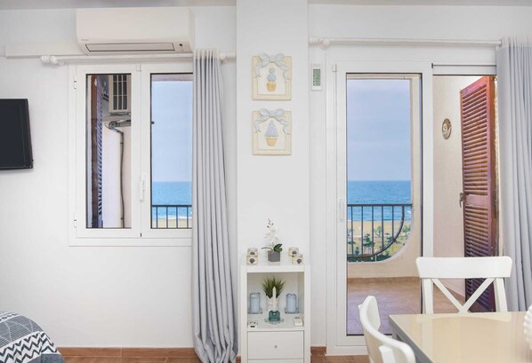 A room with a view of the sea, a white air conditioning unit, a small table, and a chair.