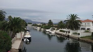 Un canal bordé de palmiers, avec des bateaux amarrés sur la rive gauche, et un bâtiment blanc avec un toit rouge sur la rive droite.