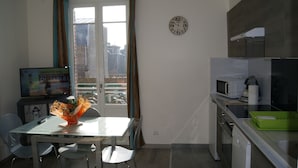 A small kitchen with a microwave, a sink, and a window with curtains. - Asylum Single Apartment (Mers-Les-Bains)