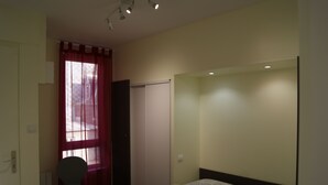 A bedroom with a bed, a chair, a window with curtains, and a door. - Asylum Single Apartment (Mers-Les-Bains)