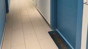 Un couloir avec des casiers, une porte bleue et un paillasson.