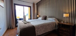 A hotel room with a bed, a nightstand with a lamp, a window with curtains, and a view of the outside. - IN FIRST LINE OF THE SEA, WITH AIR CONDITIONED POOL, PRIVATE SOLARIUM and WiFi - 30 (Tenerife)
